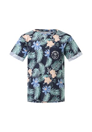 Garçon portant un T-shirt bleu marine à imprimé floral, un jean bleu, des baskets blanches, tenant des lunettes de soleil jaunes, regardant sur le côté sur un fond uni.