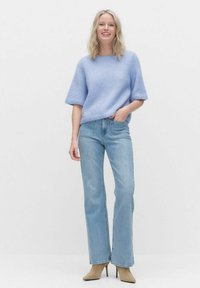 Ljusblå virkad tröja med korta ärmar, parad med ljusblå högmidjade jeans och beige klackstövlar. Enkel vit bakgrund.