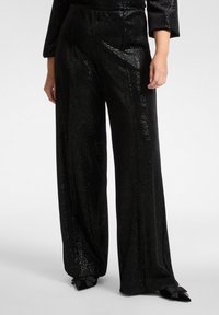 Czarne spodnie o szerokich nogawkach wykonane z błyszczącego materiału o teksturowanej powierzchni, z gładkim paskiem i subtelnymi detalami szwów. Brak widocznych kieszeni.