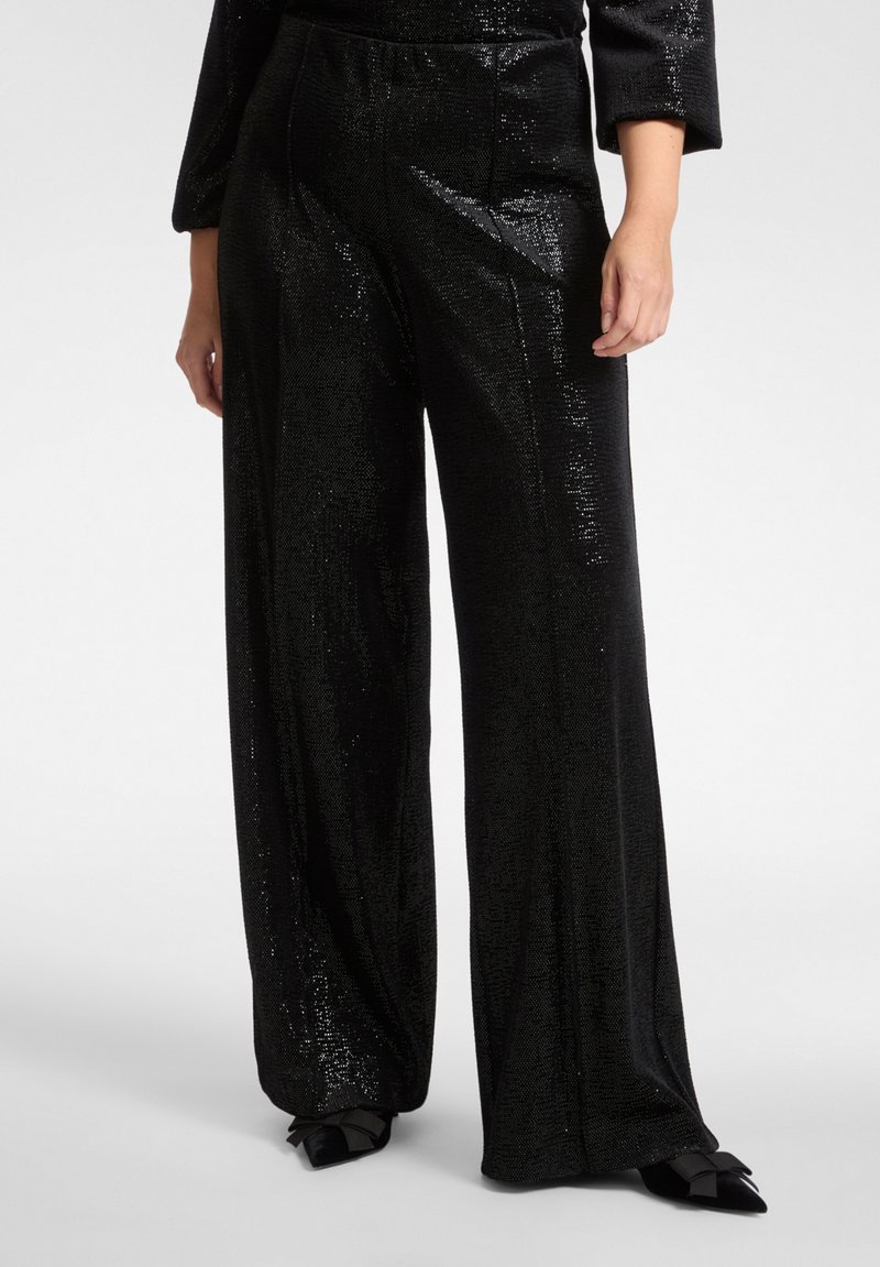Czarne spodnie o szerokich nogawkach wykonane z błyszczącego materiału o teksturowanej powierzchni, z gładkim paskiem i subtelnymi detalami szwów. Brak widocznych kieszeni.