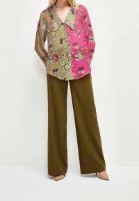 Blouse à motifs floraux en vert et rose avec un large col, associée à un pantalon taille haute vert olive et des talons beiges.