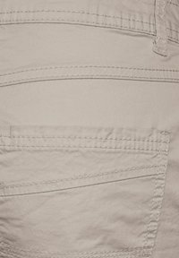 Beige kangas, jossa on sileä pinta, takatasku, jossa on näkyvät saumat ja hieman kiiltoa. Yksinkertainen muotoilu ilman kuvioita.