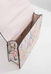 Blomsterprint håndtaske med en blød lyserød inderside, der har magnetisk lukning og guldfarvede detaljer. Lavet af tekstureret syntetisk materiale.