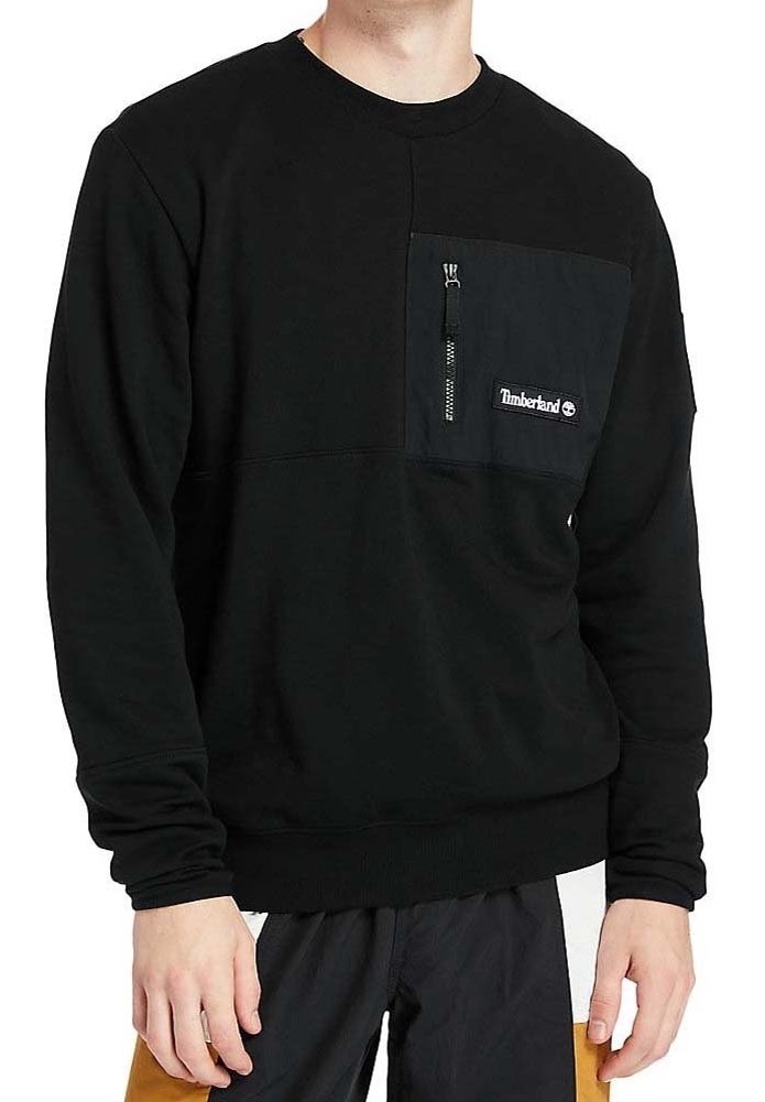 Homme portant un sweat Timberland noir avec une poche poitrine zippée et un écusson logo, debout les mains détendues le long du corps.