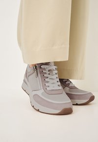 Baskets grises avec un mélange de tissu texturé et de cuir lisse, présentant des lacets blancs, une hauteur de cheville et un détail zippé sur le côté.
