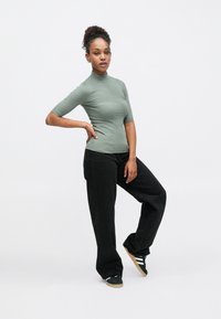 Εφαρμοστό ριμπ πλεκτό ζιβάγκο σε απαλό πράσινο, συνδυασμένο με μαύρο παντελόνι φαρδιάς γραμμής και πράσινα αθλητικά παπούτσια με επίπεδη σόλα και τρεις ρίγες.