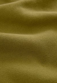 Gros plan sur un tissu vert olive texturé avec un motif tricot visible et des plis doux créant des ombres douces.