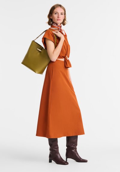 Orange, knee-length dress with a tied waist and cap sleeves; paired with dark brown knee-high boots and a green bucket bag.