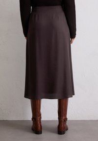 Bruine midi-rok van een soepele stof, met een eenvoudig ontwerp en een uitlopende vorm die net onder de knieën valt, gecombineerd met bruine laarzen tot de knie.