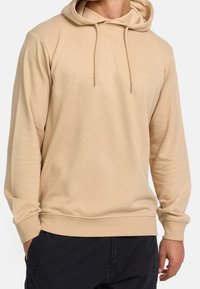 Sweat à capuche beige avec manches longues, cordons de serrage et petit logo sur la poitrine. Tissu doux avec une coupe confortable.