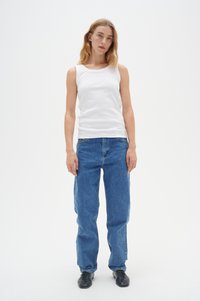 Weißes, geripptes Tanktop kombiniert mit lockeren blauen Jeans. Flache schwarze Schuhe runden das Outfit ab. Einfaches Design mit minimalen Details.
