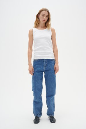White ribbed tank top paired with loose-fit blue denim jeans. Flat black shoes complete the outfit. Simple design with minimal details.