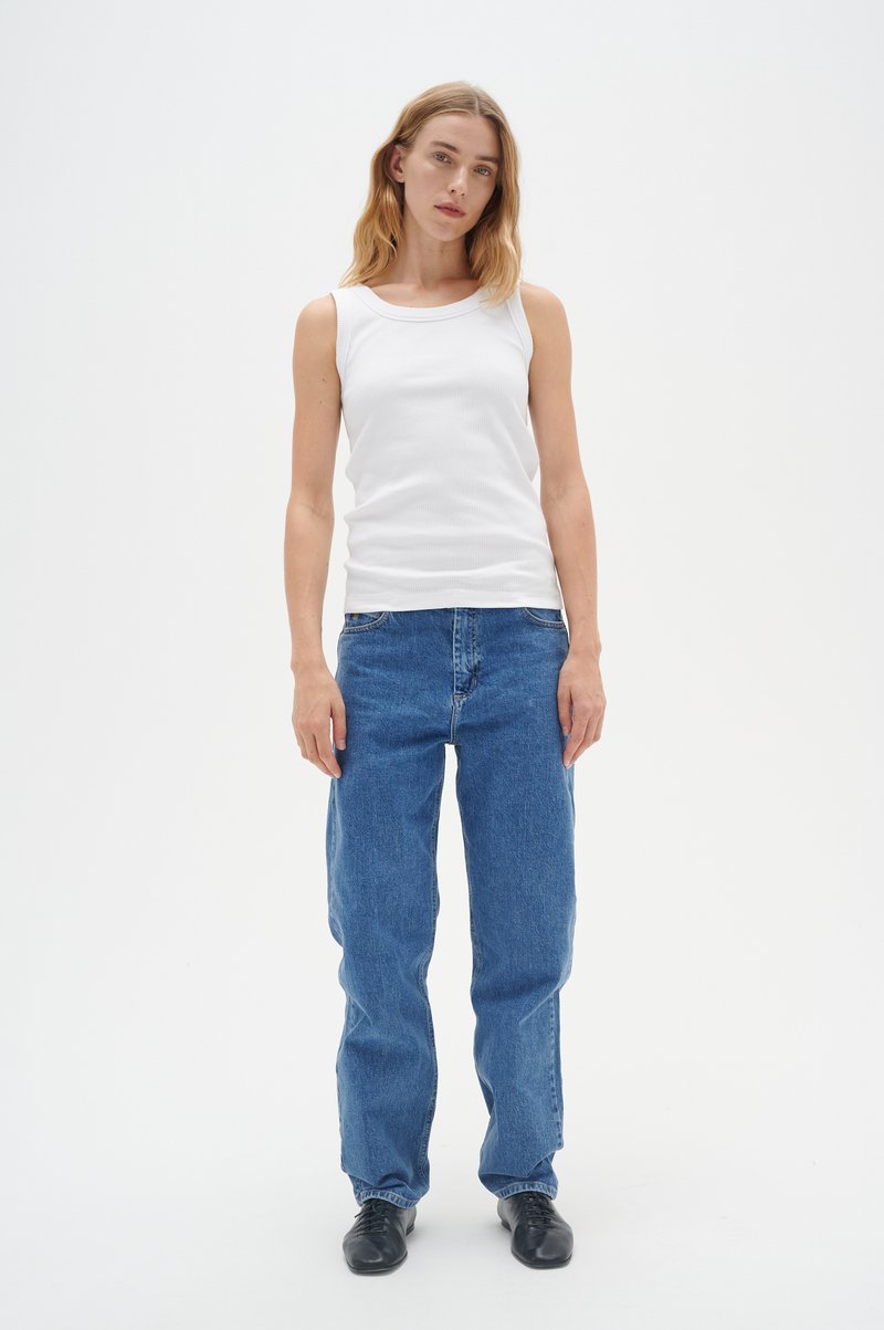 Weißes, geripptes Tanktop kombiniert mit lockeren blauen Jeans. Flache schwarze Schuhe runden das Outfit ab. Einfaches Design mit minimalen Details.