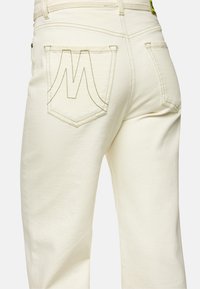 Light beige denim pants feature a unique M-shaped stitch design on the back pockets, with straight legs and a smooth texture.