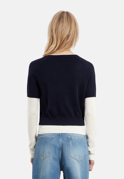 Maglione cropped navy e bianco con maniche corte, orli a coste e vestibilità aderente. Indossato su jeans in denim azzurro chiaro.