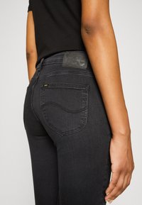 Jeans de mezclilla negra con un diseño ajustado, que cuentan con un detalle en el bolsillo trasero, un parche de logo en relieve y una textura suave.