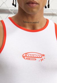 Biały top na ramiączkach z czerwoną lamówką i logo "COSMO EST 2000". Materiał wydaje się gładki i dopasowany, projekt cechuje zaokrąglony dekolt i bezrękawowy krój.