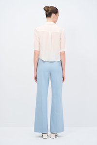 Helle, transparente Cremebluse mit kurzen Ärmeln, kombiniert mit hochtaillierten, weit geschnittenen hellblauen Hosen. Einfaches Design, glatte Textur.