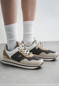 Tenisky s kombinací černé síťoviny, béžové semišové kůže a bílých akcentů. Mají texturovanou podrážku a zlaté kovové detaily na patě.