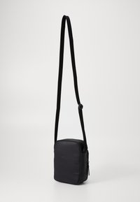 Black crossbody bag with a rectangular shape, made of smooth material. Features a long adjustable strap and a zip closure.