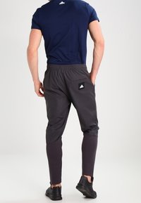 Marinblå atletisk t-shirt och mörkgrå joggers med elastisk midja; joggers har en bakficka och en svart logotypapplikation. Svarta sneakers.