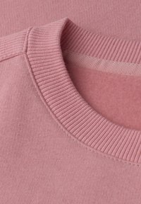 Maglione rosa chiaro con collo a girocollo a coste e una texture morbida e liscia. Il tessuto è uniforme con dettagli minimi.