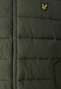 Gepolsterte Weste in olivgrün, mit einem Reißverschluss, gesteppte Bereiche und einem kleinen, gelb gestickten Adlerlogo.