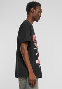 Svart bomulls T-skjorte med korte ermer, med et livlig grafisk trykk foran. Designet inkluderer sterke farger og abstrakte former.