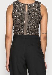 Top corto decorato con perline e un design scuro di paillettes, dotato di una cerniera centrale sul retro e un dettaglio a chiave sul collo, abbinato a pantaloni neri.