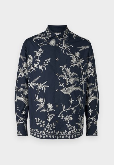 Camisa de botones azul marino con intrincados bordados blancos de flores y pájaros, de mangas largas y con cuello clásico; la tela es suave y ligera.