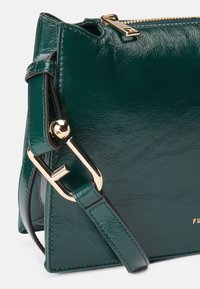 Bolsa de mão em pele sintética verde com acabamento brilhante, ferragens douradas e um design estruturado. Apresenta uma alça de ombro destacável e fecho de correr.