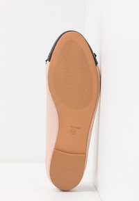 Chaussure rose avec un dessus lisse et un accent noir au niveau du talon. La semelle en caoutchouc est beige avec des rainures texturées pour une meilleure adhérence.