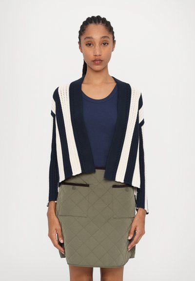 Un cardigan court à rayures bleu marine et crème avec un devant ouvert, associé à une jupe olive verte matelassée dotée de deux poches avant.