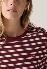 T-shirt rayé maroon avec des lignes blanches horizontales, encolure ronde et un petit logo rouge Levi's sur la partie gauche de la poitrine. Texture de tissu douce.