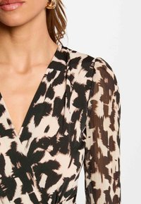 Wikkeljurk met een zwart en beige dierenprint ontwerp. Lange, doorschijnende mouwen met textuurcontrast, V-halslijn en zacht materiaal.