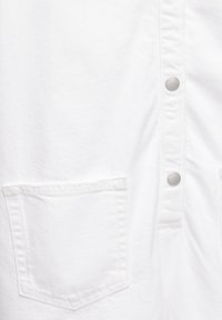 Witte katoenen kleding met zilveren knopen en een patchzak. Kenmerkt zich door een gladde textuur en een eenvoudig, knoopsluiting ontwerp.