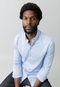 Svijetloplava košulja dugih rukava od glatkog materijala, uparena s tamnim trapericama. Pojednostavljen dizajn, bez vidljivih uzoraka ili akcenta.