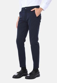 Chinos blu navy con design a gamba dritta, dotati di tasche laterali, chiusura con un bottone e tessuto di cotone morbido. Indossati con mocassini neri.