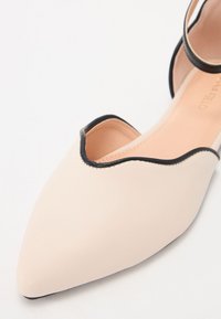 Balerini cu vârful ascuțit, din piele ecologică beige deschis, cu un design decupat și o margine contrastantă neagră. Textură netedă, cu un luciu subtil.