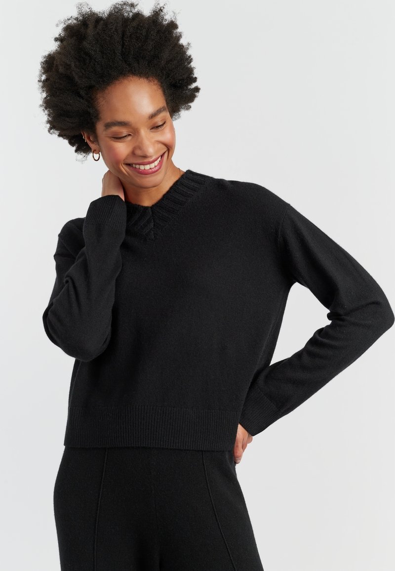 Pull en maille noir avec un col en V côtelé et des poignets. Caractérisé par un design court et une texture douce, offrant un ajustement décontracté.