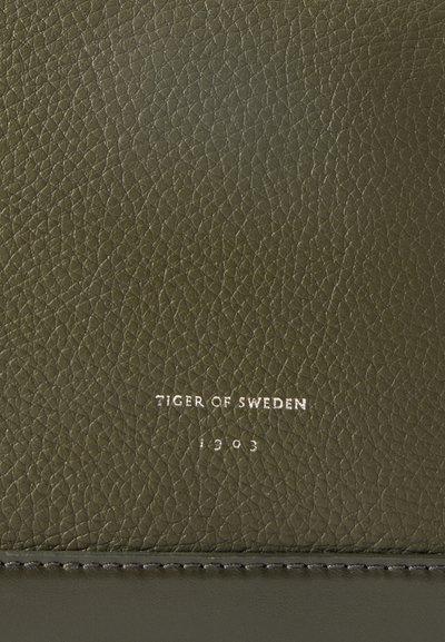 Material de pele verde com uma superfície texturizada. Apresenta texto em relevo "TIGER OF SWEDEN 1903" em prata. Detalhe de costura na parte inferior.