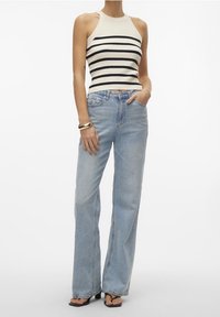 Ribbed halter top v krémové barvě s černými pruhy, kombinovaný se světle modrými širokými džínami. Model doplňuje zlatým náramkem a černými sandály.