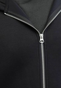Felpa nera con zip, dotata di una cerniera in metallo argentato. Il materiale sembra morbido, con una texture liscia e una vestibilità standard, presenta un cappuccio e polsini a costine.