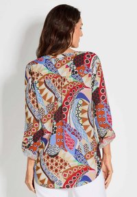 Mehrfarbige Bluse mit Muster, die eine Mischung aus geometrischen und organischen Formen zeigt, aus transparentem Stoff mit Dreiviertelärmeln und abgerundetem Saum.