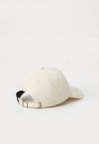 Beige színű pamut baseball sapka, ívelt napellenzővel, varrt szellőző lyukakkal és állítható pánttal, hátul fém csattal.
