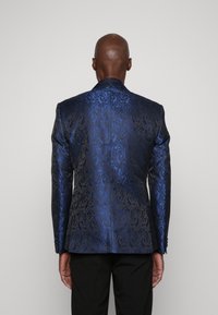 Blazer formale di colore blu scuro con intricati motivi a spirale. Presenta un taglio su misura, colletto con alette e chiusura a un bottone. Tessuto strutturato.