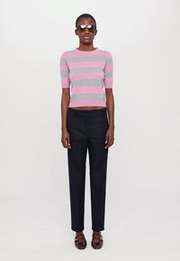 Striped kortermet strikket topp i rosa og grå, sammen med skreddersydde svarte bukser. Fottøyet har en stroppdesign.