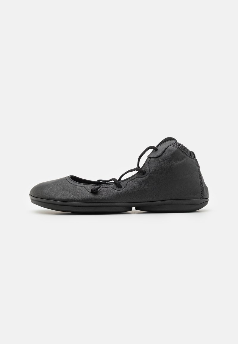 Ballerine en cuir noir avec lacets et semelle souple et flexible, vue de profil sur fond blanc.