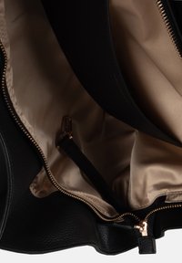 Interno di una borsa a tracolla in pelle nera con una fodera in satin beige, caratterizzata da una cerniera in oro e un attacco per cinturino interno.
