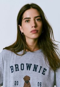 Camiseta de algodón gris con un gráfico de un perro marrón y el texto "BROWNIE" en azul oscuro, con cuello redondo y mangas cortas.